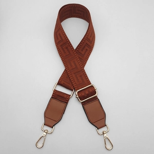 Close-up of adjustable brown woven shoulder strap with gold hardware and greek key pattern