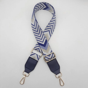 Detail of adjustable wide canvas shoulder strap with wave pattern and gold metal hooks