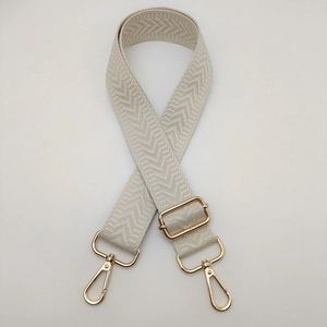 Détail d'une bandoulière beige tissée avec mousqueton doré réglable en métal poli