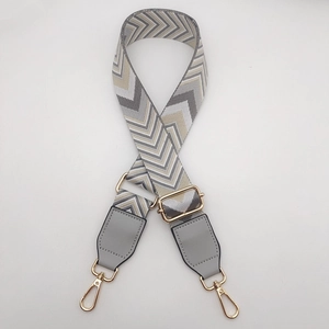 Macro shot of adjustable herringbone woven bag strap with grey faux leather and gold buckles