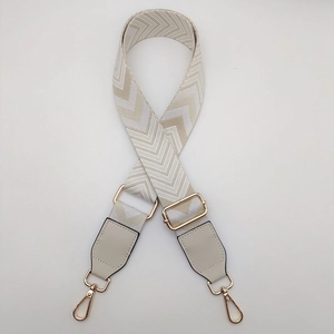 Detail of beige and white chevron canvas bag strap with gold metal hooks and leather ends