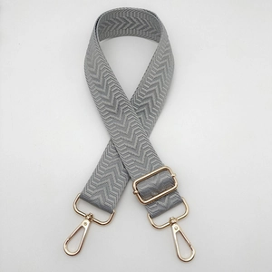 Détail de la sangle à chevrons gris avec boucles dorées et fermoirs mousquetons