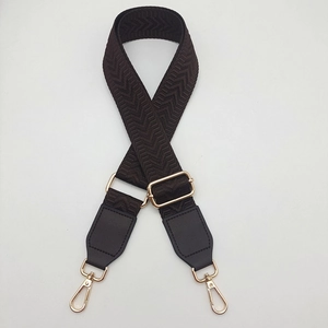 Close-up of wide herringbone webbing strap with dark brown leather ends and gold metal hooks