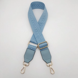 Detail of light blue adjustable canvas shoulder strap with gold metal buckles and leather ends