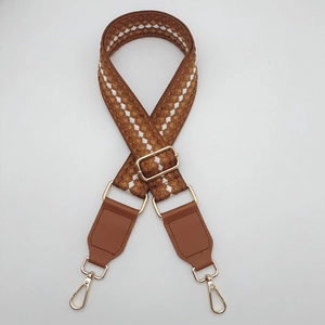Dettaglio di tracolla intrecciata con punte in pelle marrone e fibbie metalliche dorate