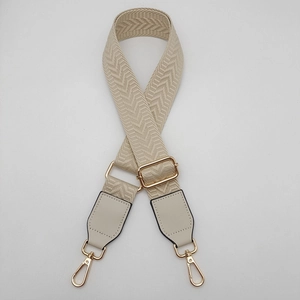 Detail of adjustable beige canvas bag strap with herringbone texture and gold metal hooks