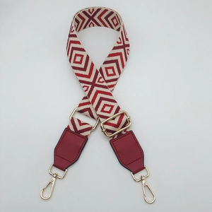 Detail of red geometric canvas shoulder strap with gold metal buckles and leather ends
