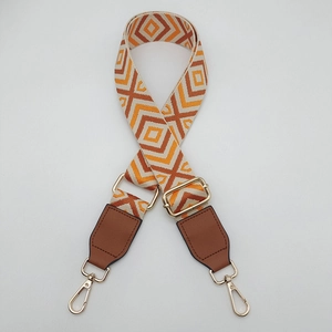 Detail of adjustable wide canvas bag strap with orange diamond jacquard and gold hooks