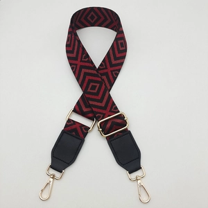 Close-up of wide red and black geometric diamond pattern canvas bag strap with gold hooks