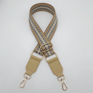 Dettaglio della tracolla tessuta geometrica con ganci oro chiaro e finiture in pelle beige
