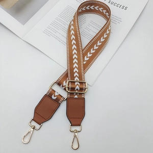Détail de la bandoulière réglable en nylon marron avec motif flèche blanche et crochets dorés