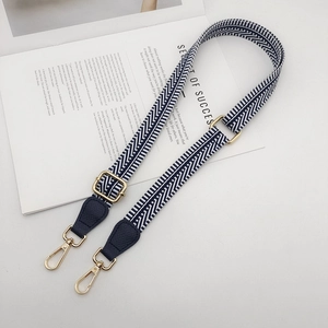 Detail of adjustable navy blue woven bag strap with golden metal hooks and leather accents