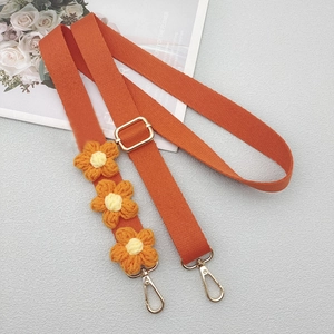 Detail of adjustable orange canvas strap with woven daisy flowers and gold hardware