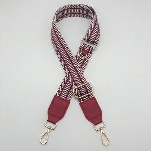 Detail of wide woven canvas bag strap with burgundy patterns and gold metal hardware