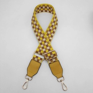Detail view of yellow checkered woven wide bag strap with gold metal lobster clasps