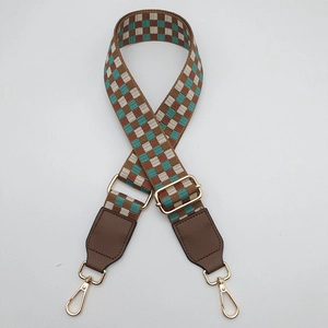 Close-up of checkered woven bag strap with brown leather ends and gold metal hooks