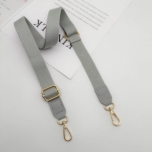 Detail of grey adjustable cotton strap with golden metal buckles and faux leather ends
