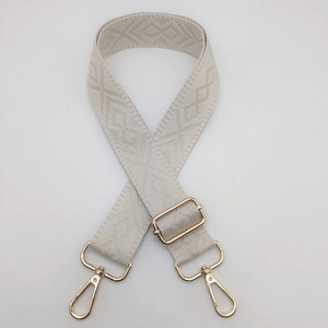 Detail of adjustable beige woven shoulder strap with geometric diamond jacquard and gold hooks