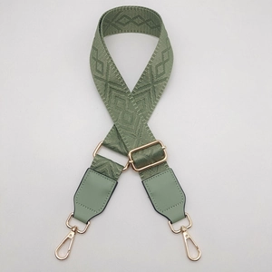 Detail of adjustable green woven shoulder strap with gold metal hooks and rhombus pattern