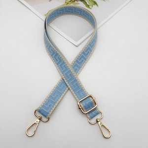 Close-up of adjustable woven bag strap with blue geometric patterns and gold metal hooks