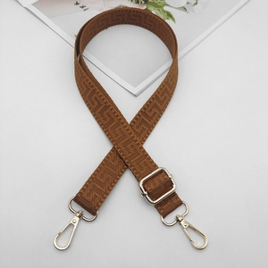 Detail of adjustable brown woven bag strap with golden hooks and geometric pattern