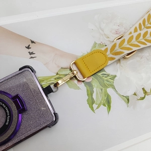 Close-up of leaf pattern woven phone strap with yellow leather ends and gold metal hooks