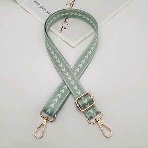 Detail of adjustable green nylon strap with white arrow pattern and gold metal hooks