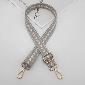 Detail view of grey nylon bag strap with white arrow pattern and golden metal buckles