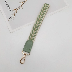 Close-up of cream wrist strap with green leaf patterns and gold metal lobster clasp