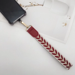 Handwoven phone wrist strap with red leaf pattern and gold metal clasp on white background