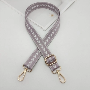 Detail of adjustable lilac purple nylon bag strap with white arrow pattern and gold metal hooks