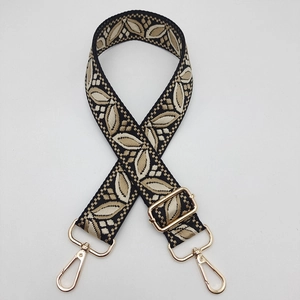 Detailed view of woven guitar style strap with gold leaf pattern and metal hardware