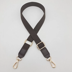 Detail of adjustable cotton webbing bag strap with gold metal hardware and faux leather ends