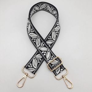 Close-up of adjustable woven bag strap with black and white leaf pattern and gold buckles