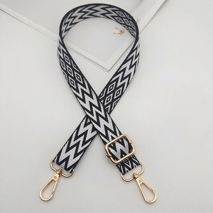 Detail of adjustable black and white geometric woven strap with golden metal hardware
