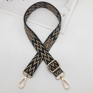 Detail of wide woven strap with black and gold geometric patterns and adjustable metal buckle