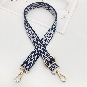 Detail of adjustable embroidered bag strap with navy geometric pattern and gold buckles