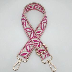Detail of adjustable wide woven bag strap with pink floral embroidery and gold metal hooks
