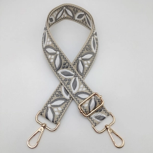 Detail of adjustable embroidered bag strap with grey leaf patterns and gold metal buckles