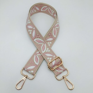 Detail of adjustable woven shoulder strap with pink floral pattern and gold metal hooks