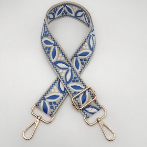 Close-up of beige canvas guitar style strap with blue floral embroidery and gold hooks