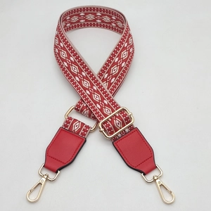 Close-up of red ethnic jacquard bag strap with geometric diamond patterns and gold hooks