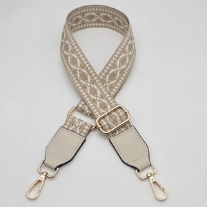 Detail of adjustable woven ethnic strap with beige geometric patterns and gold metal hooks