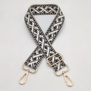 Detail view of woven geometric bag strap with polished gold-tone lobster clasps and buckles