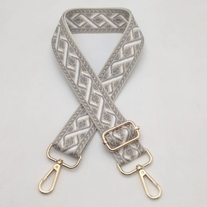 Close-up of wide jacquard bag strap with grey geometric pattern and gold metal hardware