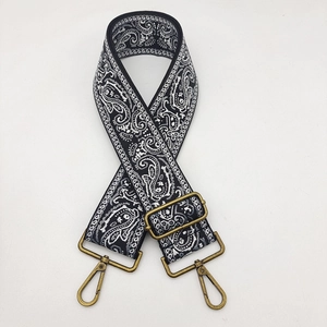 Close-up of black and white paisley embroidered bag strap with bronze metal buckles