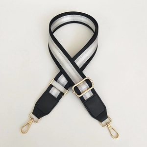Macro detail of adjustable nylon bag strap with silver metallic stripes and gold metal hooks