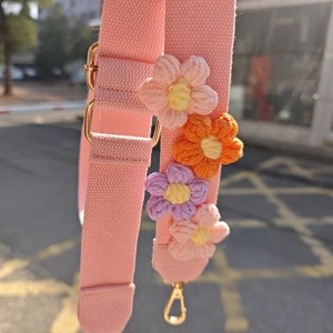 Détail de la bandoulière tricotée rose avec fleurs au crochet et boucles métalliques dorées