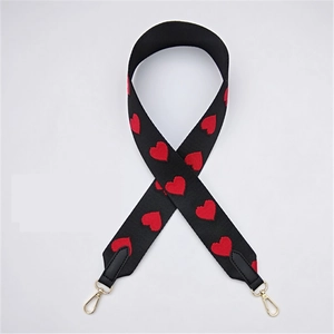 Detail of black woven bag strap featuring red heart embroidery and gold swivel hooks