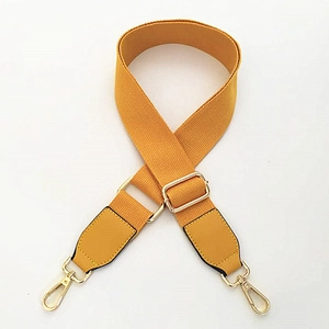 Détail de la bandoulière en toile jaune gingembre avec ferrures dorées et renfort cuir